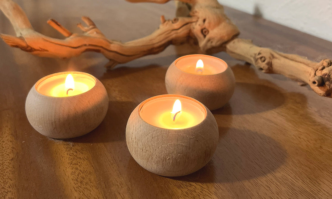 Lit Stonebriar tealight candles in wooden holders with driftwood on a wood table